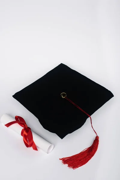Black graduation cap with red tassel and diploma on white background — Stock Photo