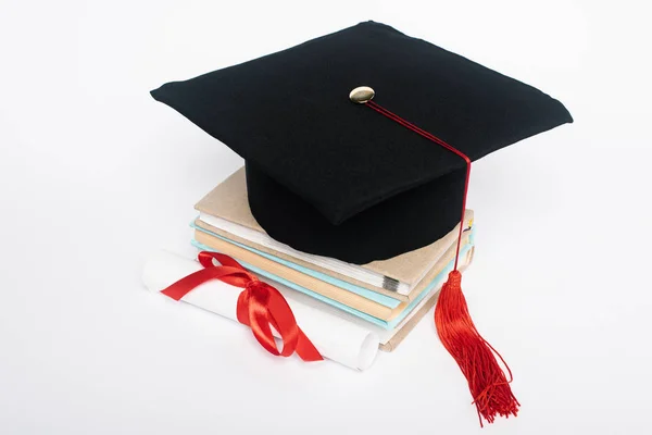 Black graduation cap with red tassel on top of books and diploma with bow isolated on white — Stock Photo