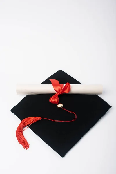 Diplom mit schöner Schleife auf schwarzer Abschlussmütze auf weißem Hintergrund — Stockfoto