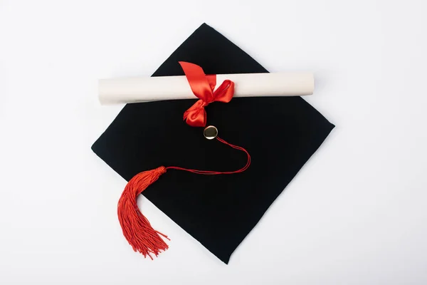 Vista superior del gorro de graduación negro con borla roja y diploma sobre fondo blanco - foto de stock