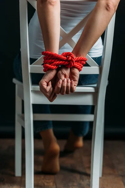 Vista cortada de mulher com as mãos amarradas na cadeira no fundo preto — Fotografia de Stock