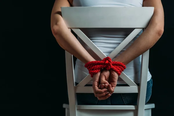 Cropped view of woman with tied hands sitting on white chair isolated on black — Stock Photo