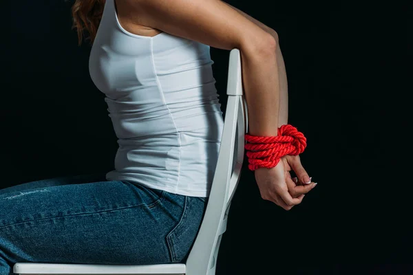 Vista cortada da mulher com as mãos amarradas na cadeira branca isolada no preto — Fotografia de Stock