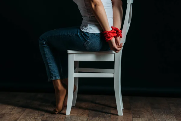 Partial view of woman with tied hands sitting on white chair on black background — Stock Photo