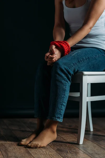 Обрезанный вид женщины со связанными руками, сидящей на стуле на черном фоне — стоковое фото