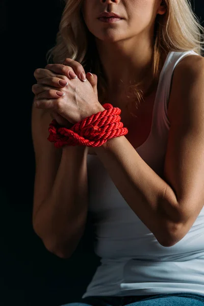 Vista parcial de las manos de mujer atadas con cuerda roja aislada en negro - foto de stock