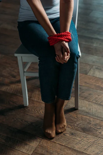 Обрезанный вид женщины со связанными руками, сидящей на стуле на деревянном фоне — стоковое фото