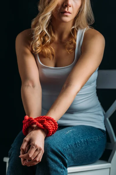 Cropped view of victim with tied hands sitting on chair isolated on black — Stock Photo