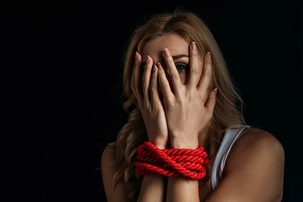 Scared victim with tied hands looking at camera through fingers isolated on black — Stock Photo