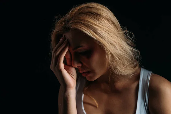 Depressed woman touching face with bruise isolated on black — Stock Photo