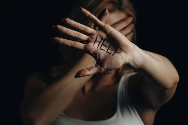 Víctima con cara oscura mostrando palma con letras de ayuda aisladas en negro - foto de stock