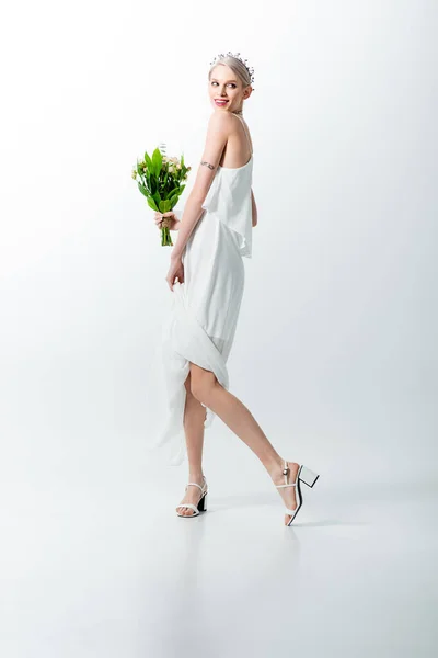 Lächelnde schöne tätowierte Braut mit posierendem Strauß auf Weiß — Stockfoto