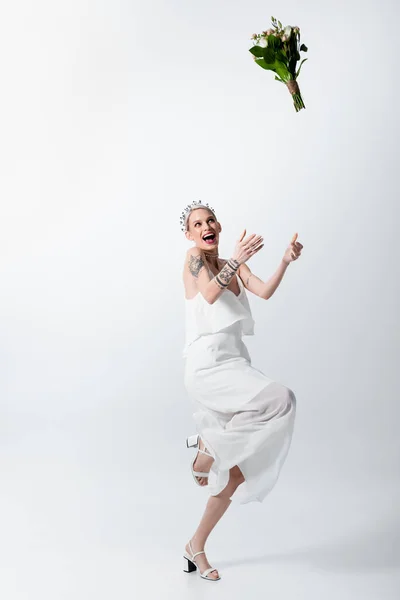 Heureuse belle mariée tatouée jetant bouquet sur blanc — Photo de stock