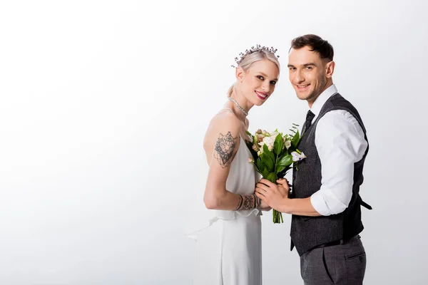 Vista laterale di sorridere bella sposa tatuata e bello sposo che tiene le mani isolate su bianco — Foto stock