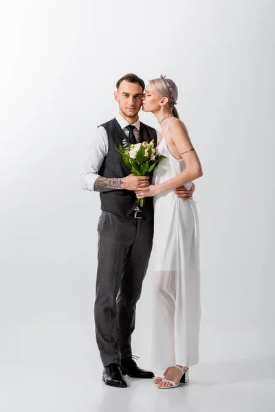 Schöne tätowierte Braut mit geschlossenen Augen küsst schönen Bräutigam auf weiß — Stockfoto