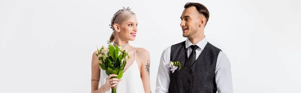 Happy beautiful tattooed bride and handsome bridegroom looking at each other isolated on white, panoramic shot — Stock Photo