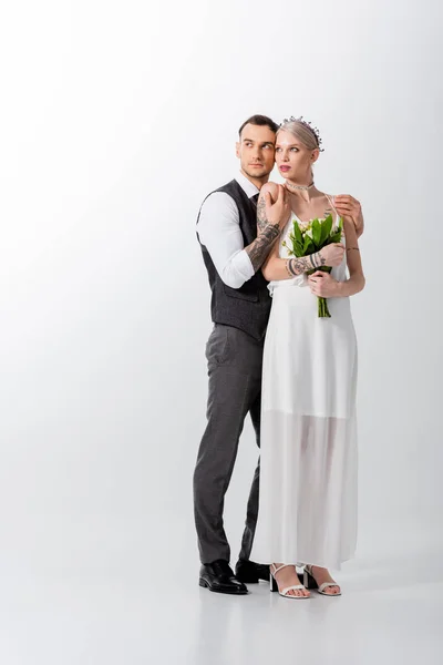 Beautiful tattooed bride and handsome bridegroom embracing on white — Stock Photo