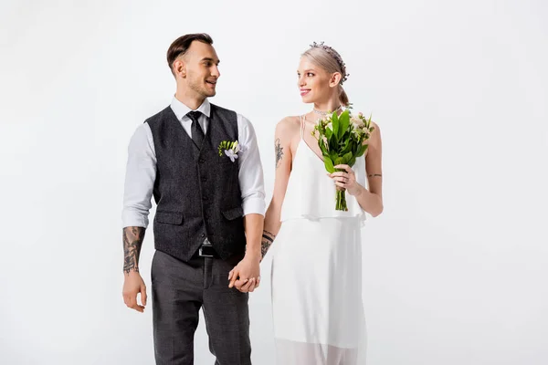 Happy beautiful tattooed bride and handsome bridegroom holding hands isolated on white — Stock Photo