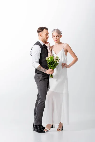 Wunderschöne tätowierte Braut mit Strauß und hübschem Bräutigam auf Weiß — Stockfoto