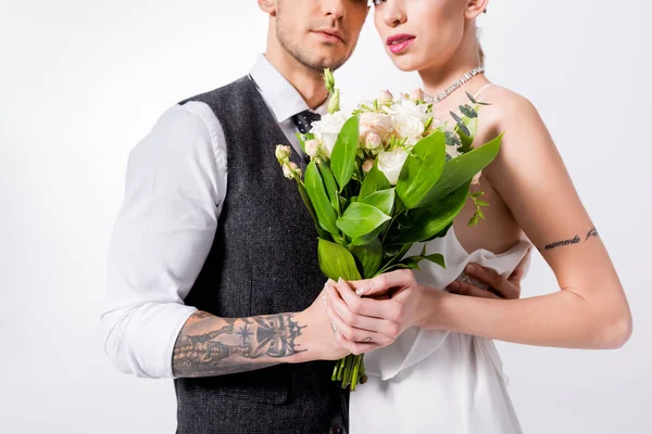 Vista ritagliata di bella sposa tatuata con bouquet e bellissimo sposo isolato su bianco — Foto stock