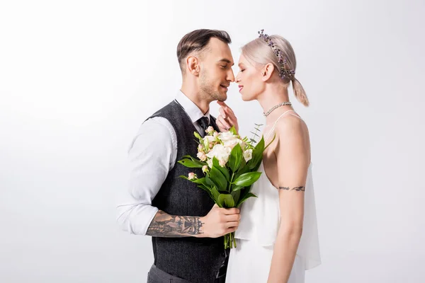 Beautiful tattooed bride and handsome bridegroom standing nose to nose isolated on white — Stock Photo