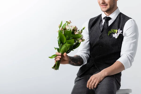 Vista cortada de sorriso tatuado elegante noivo com buquê e boutonniere no cinza — Fotografia de Stock