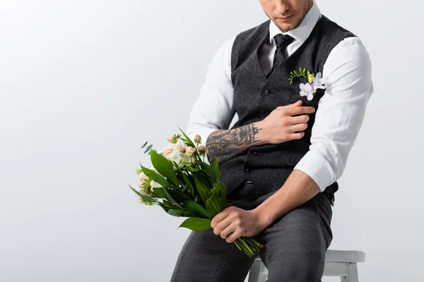 Vista cortada de noivo elegante tatuado com buquê ajustando boutonniere em cinza — Fotografia de Stock