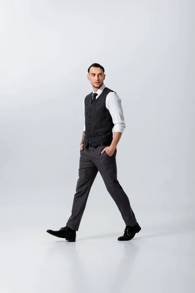 Handsome tattooed elegant bridegroom walking with hands in pockets on grey background — Stock Photo