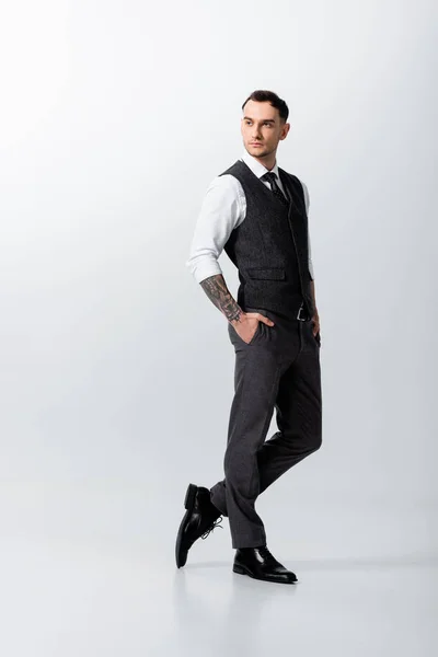 Handsome tattooed elegant bridegroom posing with hand in pocket on grey background — Stock Photo