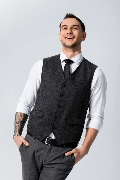 Happy handsome tattooed elegant bridegroom with hands in pockets isolated on grey — Stock Photo