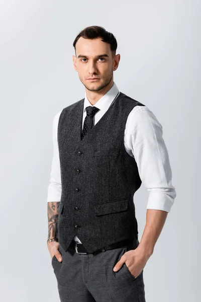 Guapo tatuado elegante novio con las manos en bolsillos aislados en gris - foto de stock