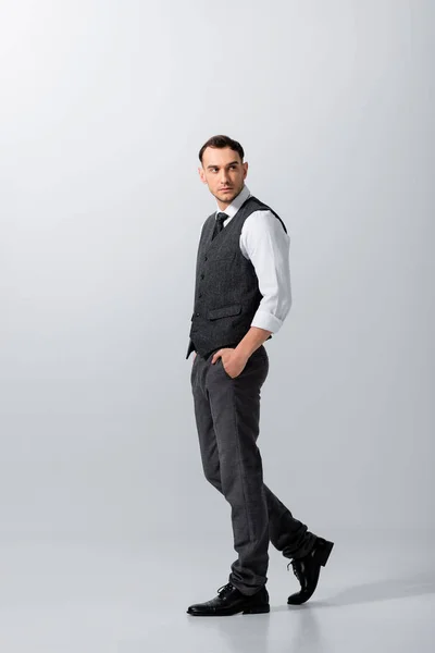 Schöner tätowierter eleganter Bräutigam, der mit den Händen in den Taschen auf grauem Hintergrund geht — Stockfoto