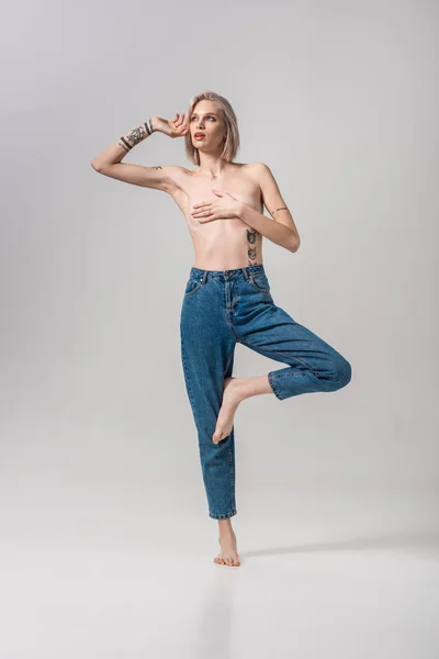 Sexy junge tätowierte Frau oben ohne bedeckt Brust mit der Hand und posiert auf grau — Stockfoto