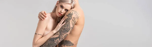 Vista lateral de jovem casal tatuado nu abraço isolado em cinza, tiro panorâmico — Fotografia de Stock