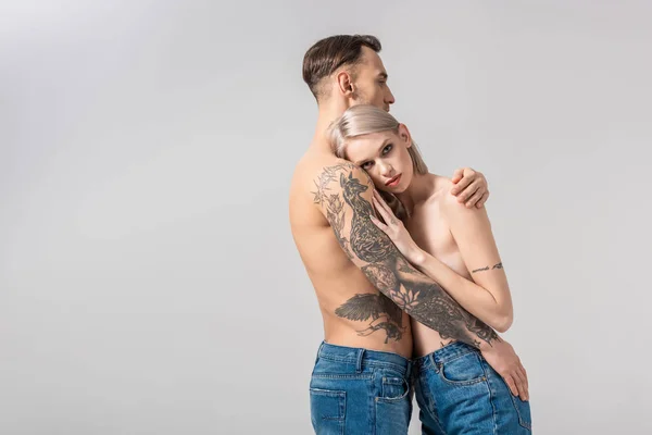 Vista laterale della giovane coppia tatuata nuda che si abbraccia isolata sul grigio — Foto stock