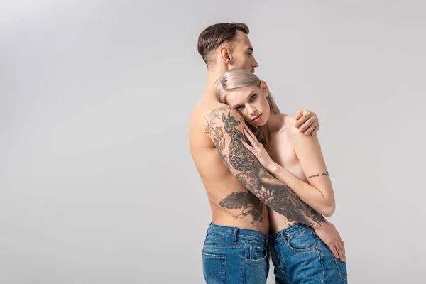 Vista lateral de jovem nu tatuado casal abraço isolado no cinza — Fotografia de Stock