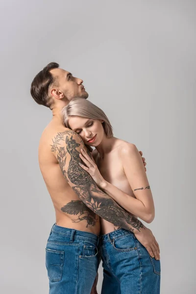 Вид збоку молода гола татуйована пара обіймається ізольовано на сірому — стокове фото