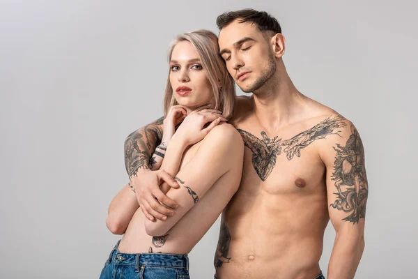 Молодая обнаженная татуированная пара обнимает изолированную серую — стоковое фото