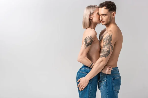 Вид збоку молода гола татуйована пара обіймається ізольовано на сірому — стокове фото