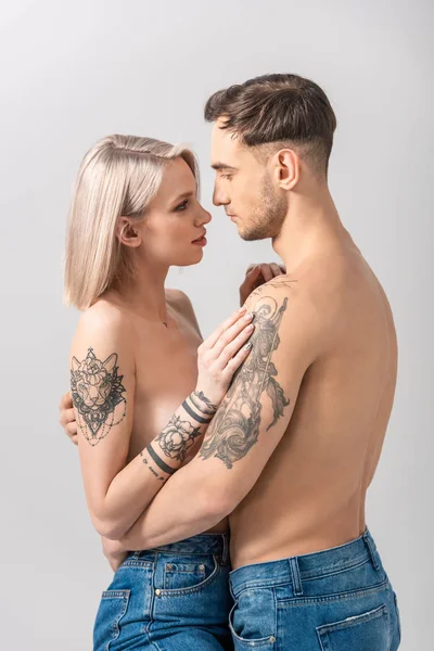 Vista lateral de jovem nu tatuado casal abraço isolado no cinza — Fotografia de Stock