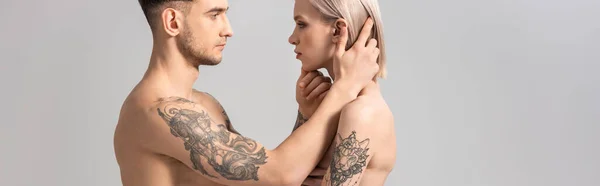 Vue latérale du jeune couple tatoué torse nu en jeans isolé sur fond gris, panoramique — Photo de stock