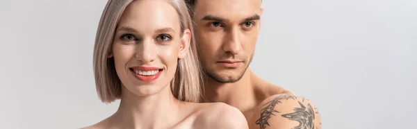 Щаслива молода гола татуйована пара обіймається ізольовано на сірому, панорамний постріл — стокове фото