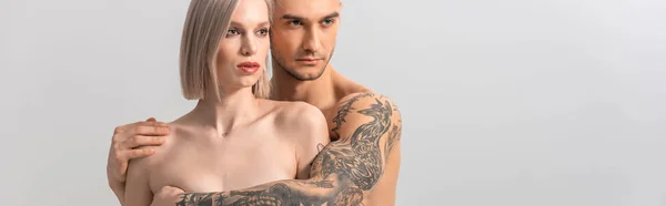 Молода гола татуйована пара обіймається ізольовано на сірому, панорамний постріл — стокове фото