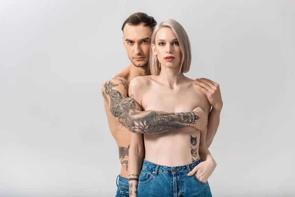 Joven sin camisa tatuado pareja en jeans abrazo aislado en gris - foto de stock