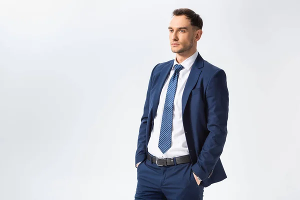 Exitoso joven hombre de negocios en traje azul con manos en bolsillos aislados en blanco - foto de stock