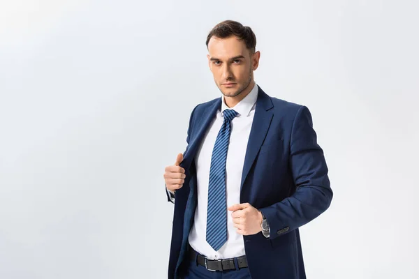 Exitoso joven hombre de negocios en traje azul con las manos en la chaqueta aislada en blanco - foto de stock