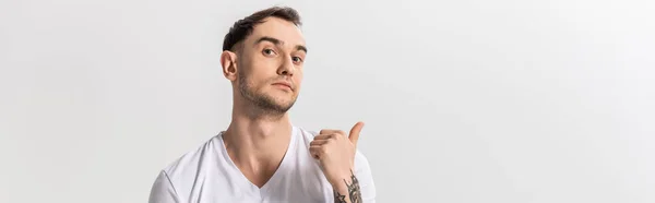 Красивый молодой татуированный мужчина, указывающий пальцем в сторону, изолированный на белом, панорамном снимке — стоковое фото