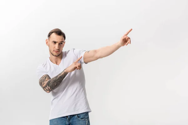 Guapo joven tatuado hombre señalando con los dedos a un lado aislado en blanco - foto de stock