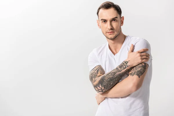 Серьезный красивый молодой татуированный мужчина со скрещенными руками, изолированный на белом — стоковое фото