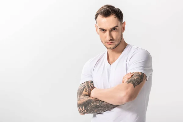 Sérieux beau jeune homme tatoué avec les bras croisés isolé sur blanc — Photo de stock